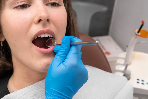 Close-up of the dentist\'s hands is performed by examining the oral cavity of a young woman with the help of a mirror. Patient with her mouth open in a dentist\'s chair