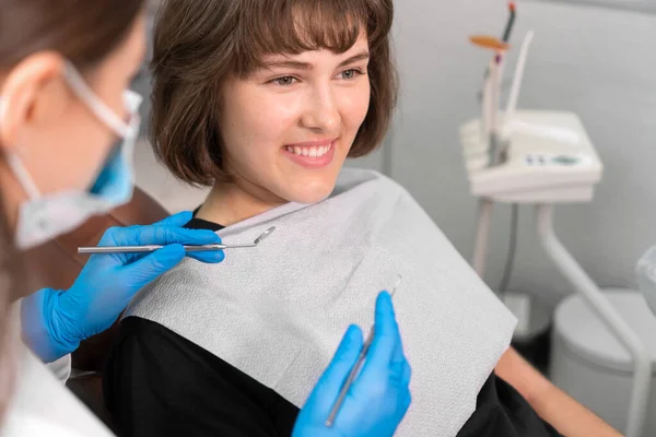 Smiling girl in dentist\'s chair looks at her doctor with confidence, and then turns her gaze directly into camera and smiles, close-up. dental treatment by professional dentist in modern clinic