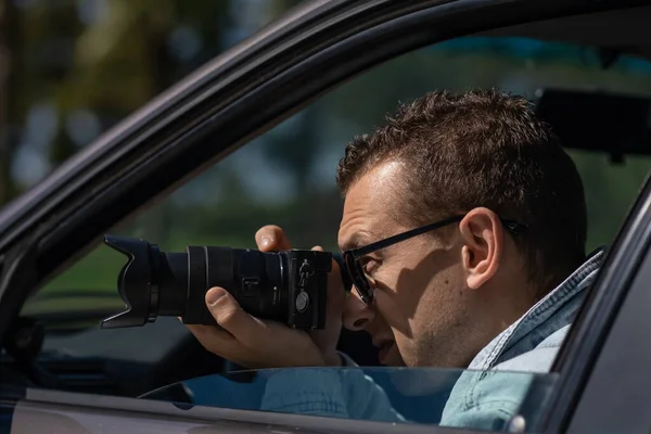カメラ付きサングラスの男は車の中に座って プロのカメラで写真を撮る 私立探偵やPaparazziスパイ ジャーナリストは感覚を求め 有名人に従う — ストック写真