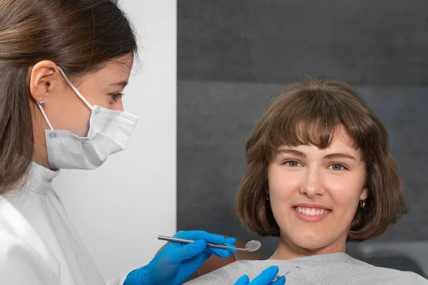 Młoda Uśmiechnięta Kobieta Siedzi Fotelu Dentystycznym Patrzy Kamerę Dentysta Trzyma — Zdjęcie stockowe