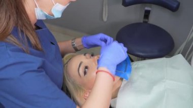Diş hekiminin elleri, dişçi pançı ve eşarplı. Dişçi, kauçuk barajla kadın dişine bakıyor. Modern diş muayenehanesi. Caries 'in tedavi ortadan kaldırılması, dolum kurulumu