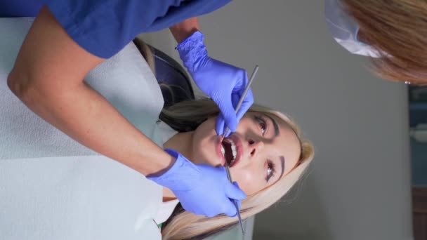 女性歯科医が歯科医院で患者の歯を検査します 医者は歯をガイド付きの歯科器具で検査し ケアのための治療を探し 充填の問題をチェックします 垂直ビデオ — ストック動画
