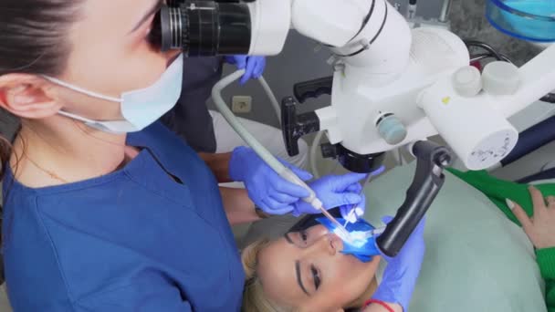 歯科顕微鏡を用いた女性歯科医歯クリニック事務所 顕微鏡を使った経験豊富な歯科医による治療を受けています 歯医者さんの椅子の上の女性のイメージ — ストック動画