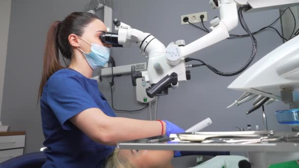 女牙医用牙科显微镜治疗病人牙科诊所办公室 用显微镜接受有经验牙医的治疗 牙医办公室病人椅子上的女性形象 — 图库视频影像