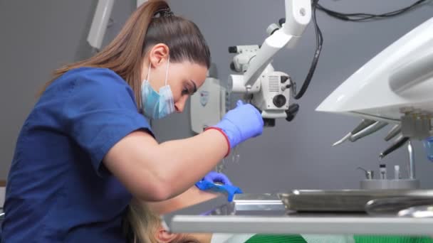 歯のパンチとコファダムスカーフで手袋の歯科医の手 歯医者はゴムダムで患者に女性の歯を扱います 近代的な歯科事務所 介護の排除 充填の設置 — ストック動画