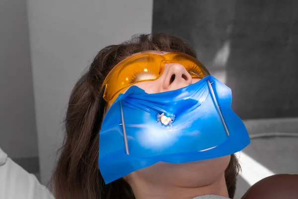 歯科治療のために保護ガラスを身に着けている彼女の顎に設置されたコファダムを持つ若い患者 歯を隔離するために歯科ダムを使用して歯科医 — ストック写真