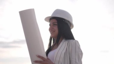 Kadın inşaat mühendisi. Kağıda çizim yapan bir mimar. Genç kadın arka plandaki şantiyeye bakıyor. İnşaat konsepti. Doğrulama ve planlama, profesyonel faaliyet.