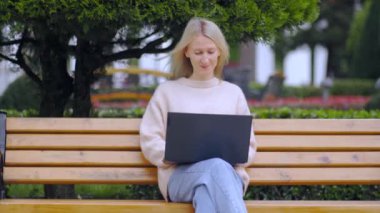 Parkta dizüstü bilgisayarda çalışan ve güneşli bir günde bankta oturan bir kadın. Mobil Ofis. Serbest ticaret konsepti. Business Lady Works. Öğrenci sınavlara hazırlanıyor. Gazeteci..