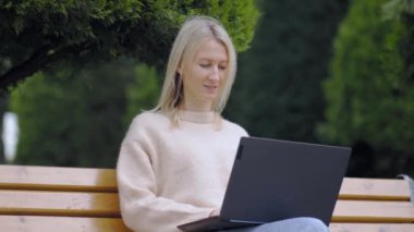 Çevrimiçi iş kadını. Genç bir kadın dizüstü bilgisayarla kentteki bankta oturuyor, yazı yazıyor ve güneşli bir günde çalışıyor. Eğitim kavramı. Serbest çalışan biri. Sınav hazırlığı için öğrenci dizüstü bilgisayarı