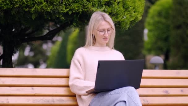オンラインビジネスウーマン 若い女性はノートパソコンを通して市内のベンチに座ってテキストを入力し 晴れた日に働いています 教育の概念 フリーランサー 試験準備のための学生のラップトップコンピュータ — ストック動画