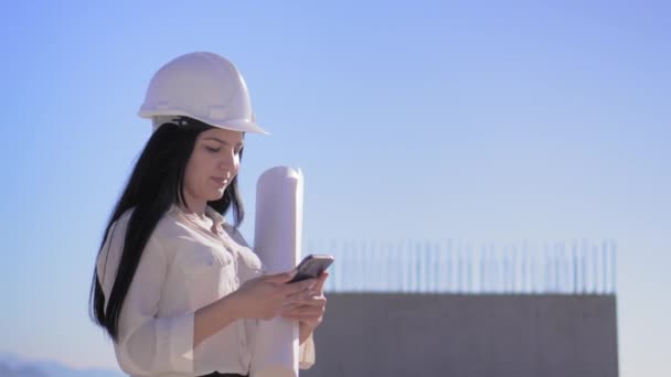 Vrouwelijke Architect Bouwplaats Helm Houdt Mobiele Telefoon Gevouwen Papieren Plan — Stockvideo