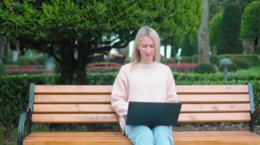 Parkta dizüstü bilgisayarda çalışan ve güneşli bir günde bankta oturan bir kadın. Mobil Ofis. Serbest ticaret konsepti. Business Lady Works. Öğrenci sınavlara hazırlanıyor. Gazeteci..