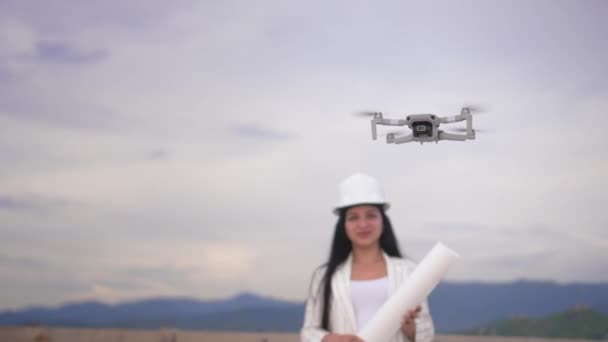 土地区画および建設プロジェクトの建設現場上の土木工学無人航空機 若いです美しい女性エンジニアで背景にヘルメット — ストック動画