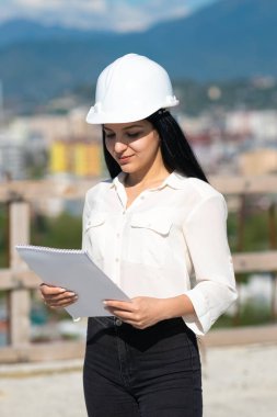 Bir inşaat alanında kağıt tabletle çalışırken kasketli genç bir kadın mimar. İnşaat alanında çalışırken koruyucu kask takan bir müfettiş. Başarılı müfettiş..