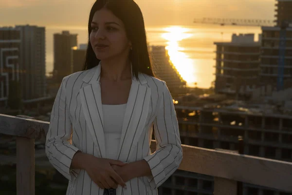 Beautiful young business woman on a construction site against the background of the sea and sunset. Concept of the construction industry, professions, construction business