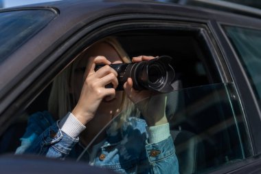 Güneş gözlüklü genç sarışın kadın arabada otururken profesyonel bir kamerayla fotoğraf çekiyor. Gazetecilik kavramı, dedektif, papparation