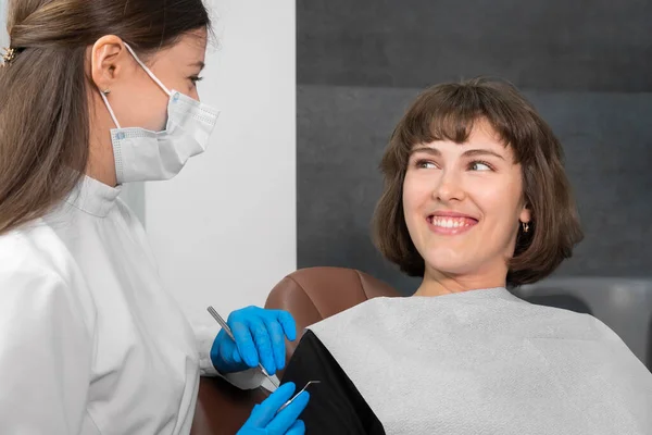 Młoda Uśmiechnięta Kobieta Siedzi Krześle Dentystycznym Patrzy Dentystę Który Trzyma — Zdjęcie stockowe