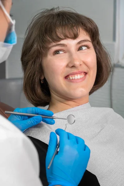 Młoda Uśmiechnięta Kobieta Siedzi Krześle Dentystycznym Patrzy Dentystę Który Trzyma — Zdjęcie stockowe