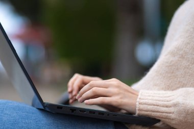 Profesyonel bir kullanıcının, dizüstü bilgisayarında yazı yazan, bankta oturan bir çalışanın kadın ellerine yakın çekim. Öğrenci, parkta dizüstü bilgisayarı olan serbest çalışan biri.