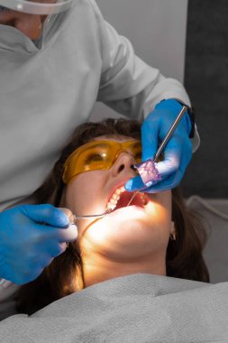 Diş hekimi, tedavi sonrası doğal ısırık ihlallerini eklem kağıdıyla kontrol ediyor. Kurulumdan sonra mührün ayarlanması. Dikey fotoğraf