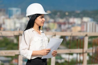 Bir inşaat alanında kağıt tabletle çalışırken kasketli genç bir kadın mimar. İnşaat alanında çalışırken koruyucu kask takan bir müfettiş. Başarılı müfettiş..
