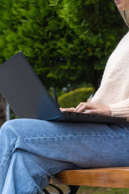 Parktaki bankta otururken dizüstü bilgisayarda yazan tanınmayan genç bir bayanın yakın çekim görüntüleri. Dikey fotoğraf