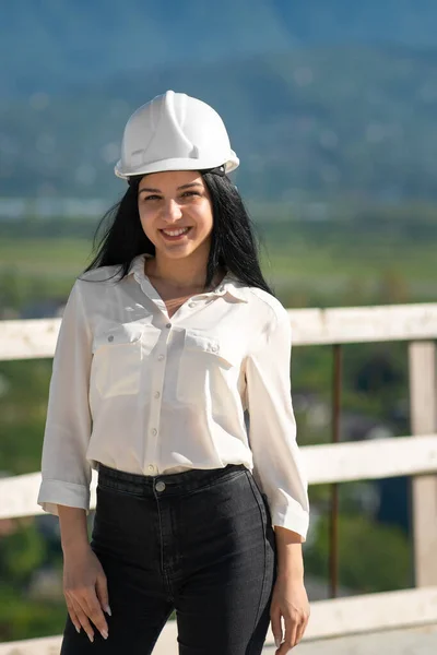 面带微笑 头戴硬礼帽的女工程师在建筑工地上看着摄像机 在建筑工地工作时戴防护头盔的主管 — 图库照片