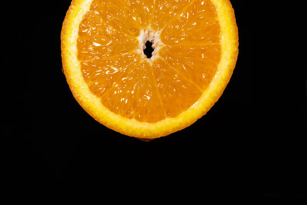 Close-up of a juicy slice of orange on a black background, macro photography. Fruity citrus background, copy space