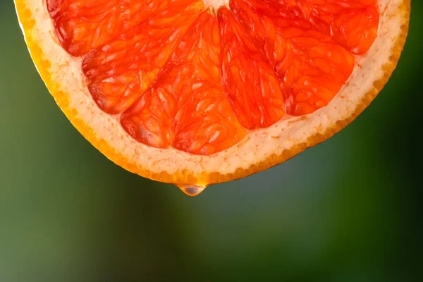 Red grapefruit juice or essential oil dripping from a fresh slice on a blurry green background, macro photography. Fruit background