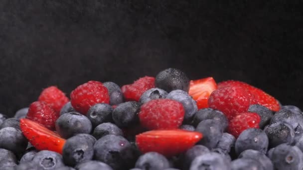 覆盆子和草莓在它们的轴上旋转着 它们被喷出水滴以雨的形式 多汁的浆果黑色背景与空间文字 浆果的混合物 — 图库视频影像