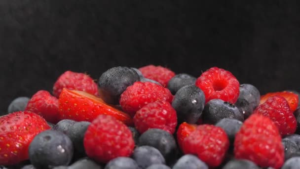 覆盆子和草莓在它们的轴上旋转着 它们被喷出水滴以雨的形式 多汁的浆果黑色背景与空间文字 浆果的混合物 — 图库视频影像