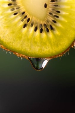 Bulanık yeşil arka planda bir damla su veya meyve suyu ile bir dilim kivi yakın plan, makro fotoğrafçılık. Meyve arkaplanı. Dikey fotoğraf