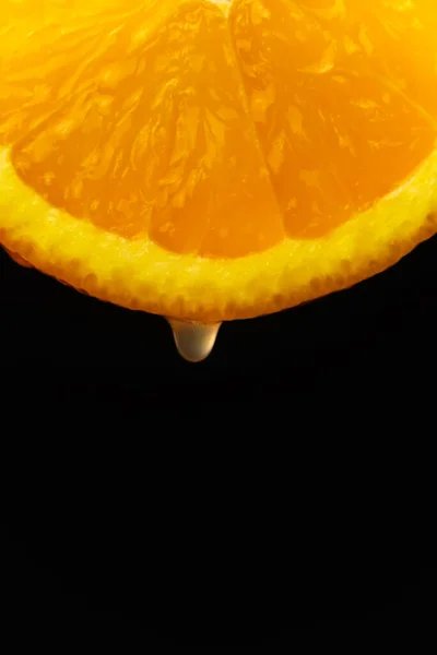 黒い背景にオレンジ色のスライスから落ちるジュースの一滴のマクロ写真 フルーツの背景 縦の写真 — ストック写真