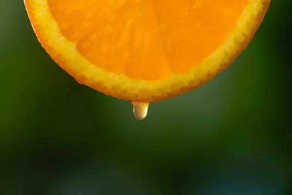 マクロ写真 鮮やかな緑色の背景にオレンジ色のスライスからドロップジュース フルーツの背景 — ストック写真
