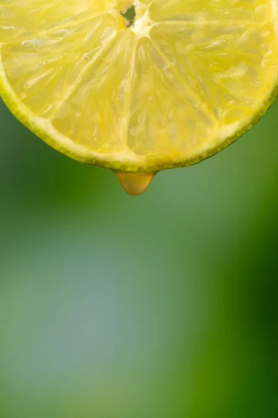 マクロ写真 緑色のぼやけた背景にジュースを一滴入れた熟したライムのスライス フルーツの背景 縦の写真 — ストック写真