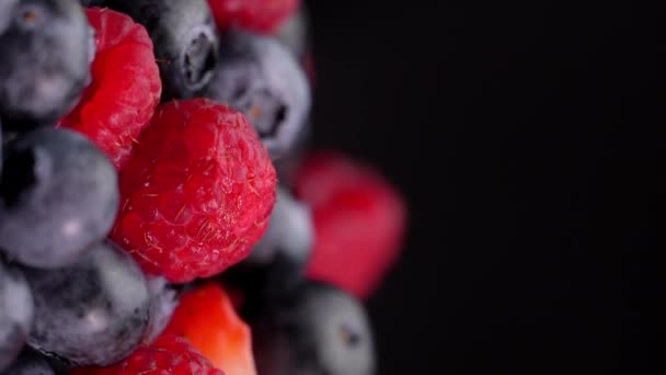 覆盆子和草莓在它们的轴上旋转着 黑色背景上的多汁浆果 有文字的空间 混合着新鲜的夏天浆果的芬芳 红黑健康 — 图库视频影像
