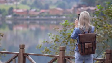 Sırt çantalı, kot elbiseli, Türkiye 'de Uzungol Gölü' nün güzel fotoğraflarını çeken güzel sarışın bir kadın. Yolculuğa susamışlık, dikiz aynası. Blogger Sosyal Ortamı.