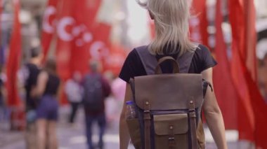 Arka plan Mutlu turist sarışın kadın sırt çantasıyla yaşlı Türk kırmızı bayraklarında yürüyor. Turist gezginleri ilginç yerler ve popüler gösteriler keşfediyor ve eski İstanbul kentinde geziniyor