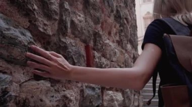 Sırt çantalı genç sarışın kadın güneşli bir günde seyahat ederken antik taş duvarlara dokunuyor. İstanbul, Türkiye 'deki Galata Kulesi' nin duvar arkasındakine yakın plan kadın eli