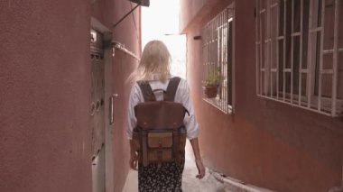 Genç, güzel, narin bir kadın işlek şehir caddesinde yürüyor. Şık seyahat kıyafetleri içinde turist, beyaz gömlek ve sırt çantasıyla gezer, yeni yerler ve sokaklar keşfeder..