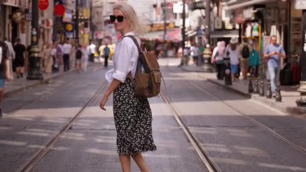 白いシャツのバックパックの若い美しいスレンダーの女性は 路面電車 鉄道が旅行している路上でトルコの通りを歩いています 群衆や街を探索する人々に対して イスティカライ — ストック動画