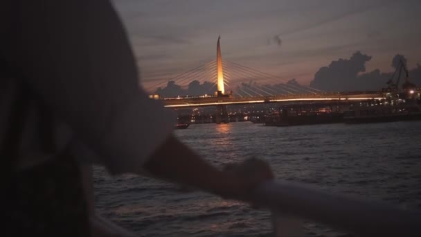 晚上或晚上在伊斯坦布尔轮渡上 在博斯普鲁斯港放松的时候 女性的亲密手都会失去焦点 女孩在船上 以桥为背景的城市的波浪和灯光 土耳其的观光船 — 图库视频影像