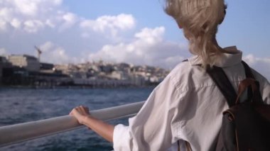 İstanbul 'da feribotta güneş gözlüklü sarışın, güzel iş kadını. Boğaz' a sürtünüyor. Beyaz tişörtlü kız gemiye biniyor. Tekne gezisi. Dalgalar arka planda. Tekneyle şehri gezmek.