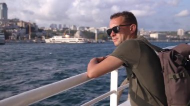 İstanbul 'da feribotta güneş gözlüklü yakışıklı bir adam boğazın üzerinde dinleniyor. Gemide sırt çantalı bir gezgin. Tekne. Dalgalar arka planda. Tekneyle şehri gezmek.