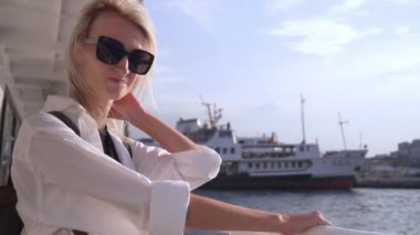 İstanbul 'da feribotta güneş gözlüklü sarışın, güzel iş kadını. Boğaz' a sürtünüyor. Beyaz tişörtlü kız gemiye biniyor. Tekne gezisi. Dalgalar arka planda. Tekneyle şehri gezmek.
