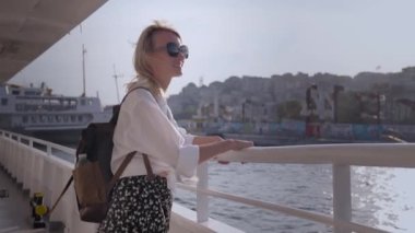 İstanbul 'da feribotta güneş gözlüklü sarışın, güzel iş kadını. Boğaz' a sürtünüyor. Beyaz tişörtlü kız gemiye biniyor. Tekne gezisi. Dalgalar arka planda. Tekneyle şehri gezmek.