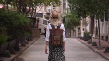 Yavaş çekim beyaz gömlekli ve hasır şapkalı güzel bayan turist eski turistik bölgede boş caddede yürüyor ve tatilinin tadını çıkarıyor. Popüler turizm merkezini gezmek.