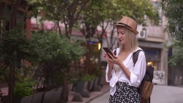 スマートフォンでアプリを勉強するサルーン帽子と琉球ザクロムの女性観光客 都市の地図またはタクシー ホテルを呼び出すこと 宿泊施設 アプリのコンセプト 旅行ソフトウェアを見つける ジョイフルツーリスト — ストック動画