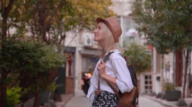 Beyaz tişörtlü, beyaz şapkalı, şehir sokaklarını zevkle seyreden güzel beyaz tenli turist kadın. Kız gezer ve yerel eğlenceleri keşfeder. Etrafına bakıp gülümsüyor.