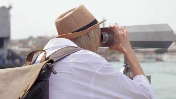 サルーン帽子とバックパックの若い観光客は 硬貨で双眼鏡を通して都市を見ます ボスフォラスの船やボートを通過するイスタンブールの望遠鏡で白人の若い幸せな女性旅行者 — ストック動画